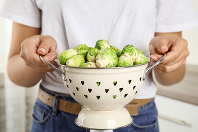 Photo of Woman holding colander with Brussels sprouts on blurred background, closeup