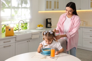 Young mother helping her little child get ready for school in kitchen