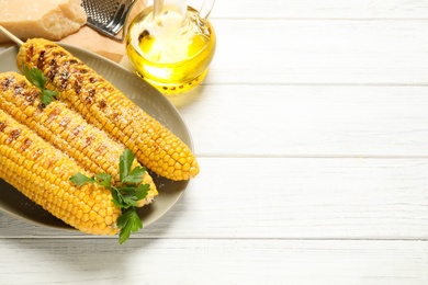 Tasty grilled corn on white wooden table, above view. Space for text