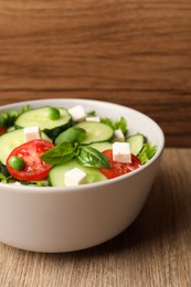 Photo of Tasty fresh salad with cucumber in bowl on wooden table, closeup