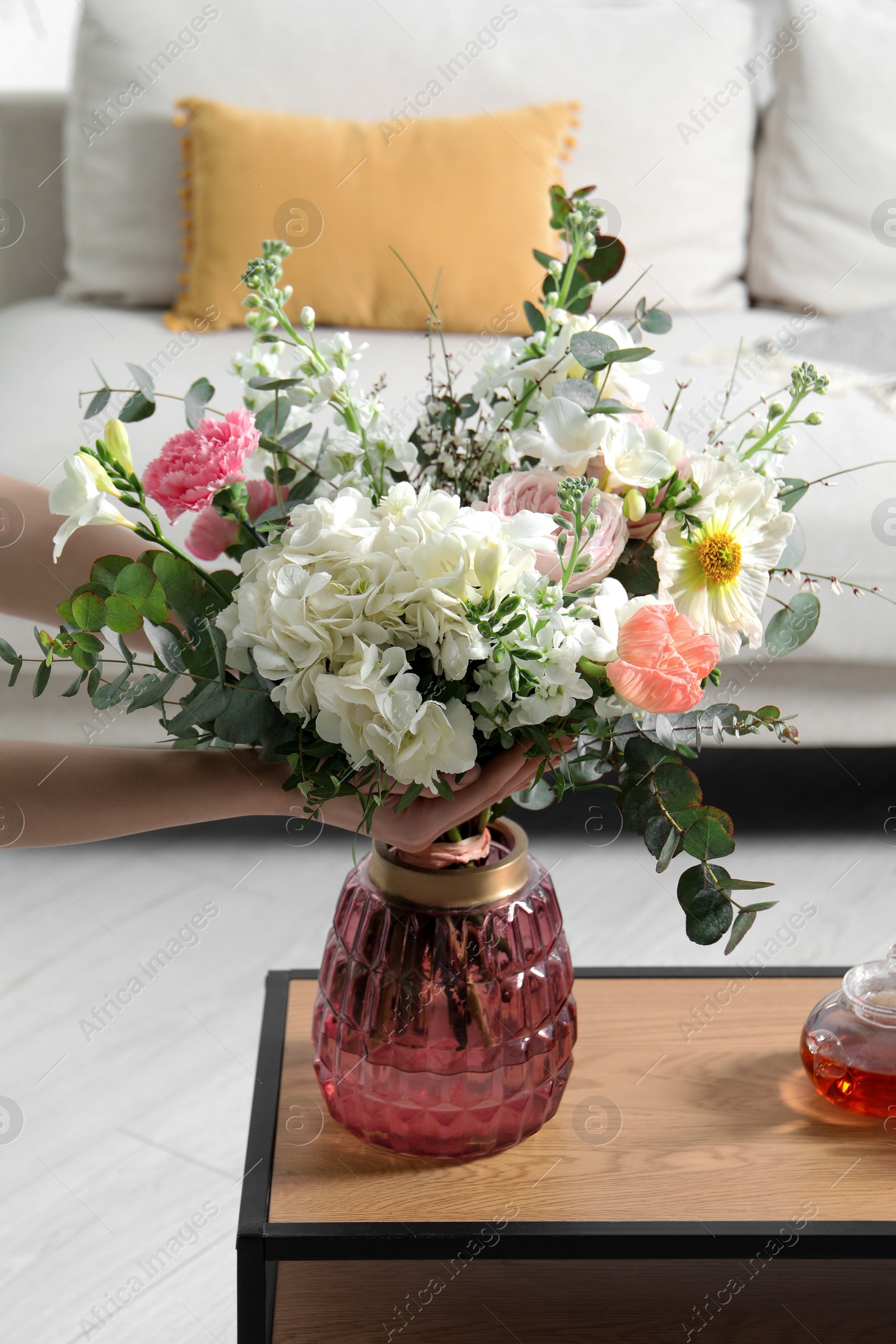 Photo of Woman arranging bouquet of beautiful flowers in vase indoors, closeup