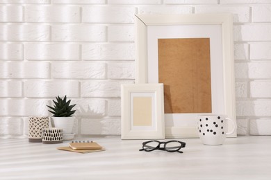 Photo of Stylish office workplace. Decor elements, glasses, cup and notebooks on white table near brick wall