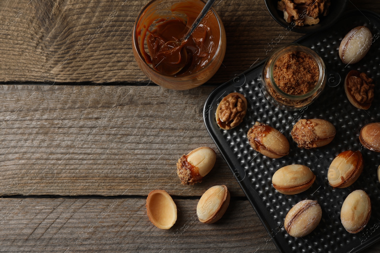 Photo of Freshly baked homemade walnut shaped cookies, boiled condensed milk and nuts on wooden table, flat lay. Space for text