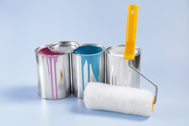 Photo of Cans of paints and roller on light blue background