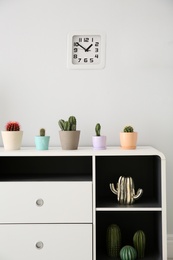 Beautiful cacti in flowerpots on white cabinet indoors