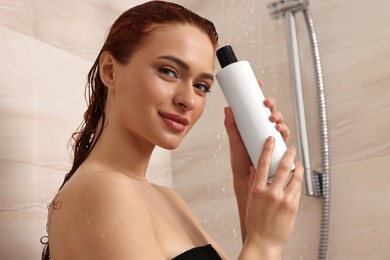 Happy young woman with bottle of shampoo in shower