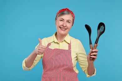 Happy housewife with spoons on light blue background