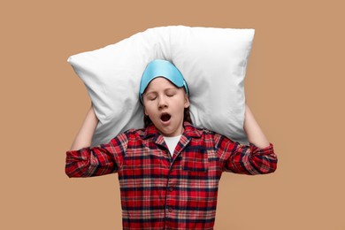 Photo of Girl with sleep mask and pillow yawning on beige background. Insomnia problem