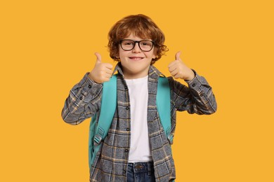 Photo of Happy schoolboy with backpack showing thumbs up gesture on orange background