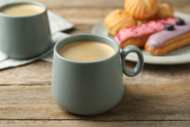 Photo of Aromatic coffee in cups, tasty eclairs and profiteroles on wooden table