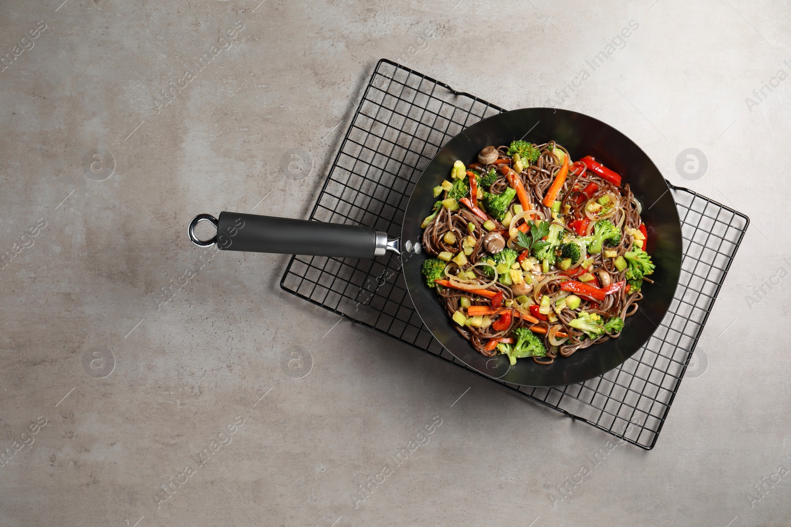 Photo of Stir-fry. Tasty noodles with meat and vegetables in wok on grey textured table, top view