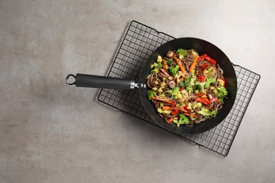 Photo of Stir-fry. Tasty noodles with meat and vegetables in wok on grey textured table, top view