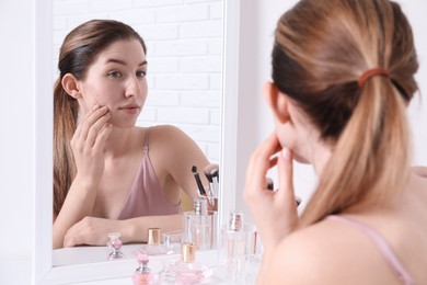 Woman with acne problem near mirror indoors