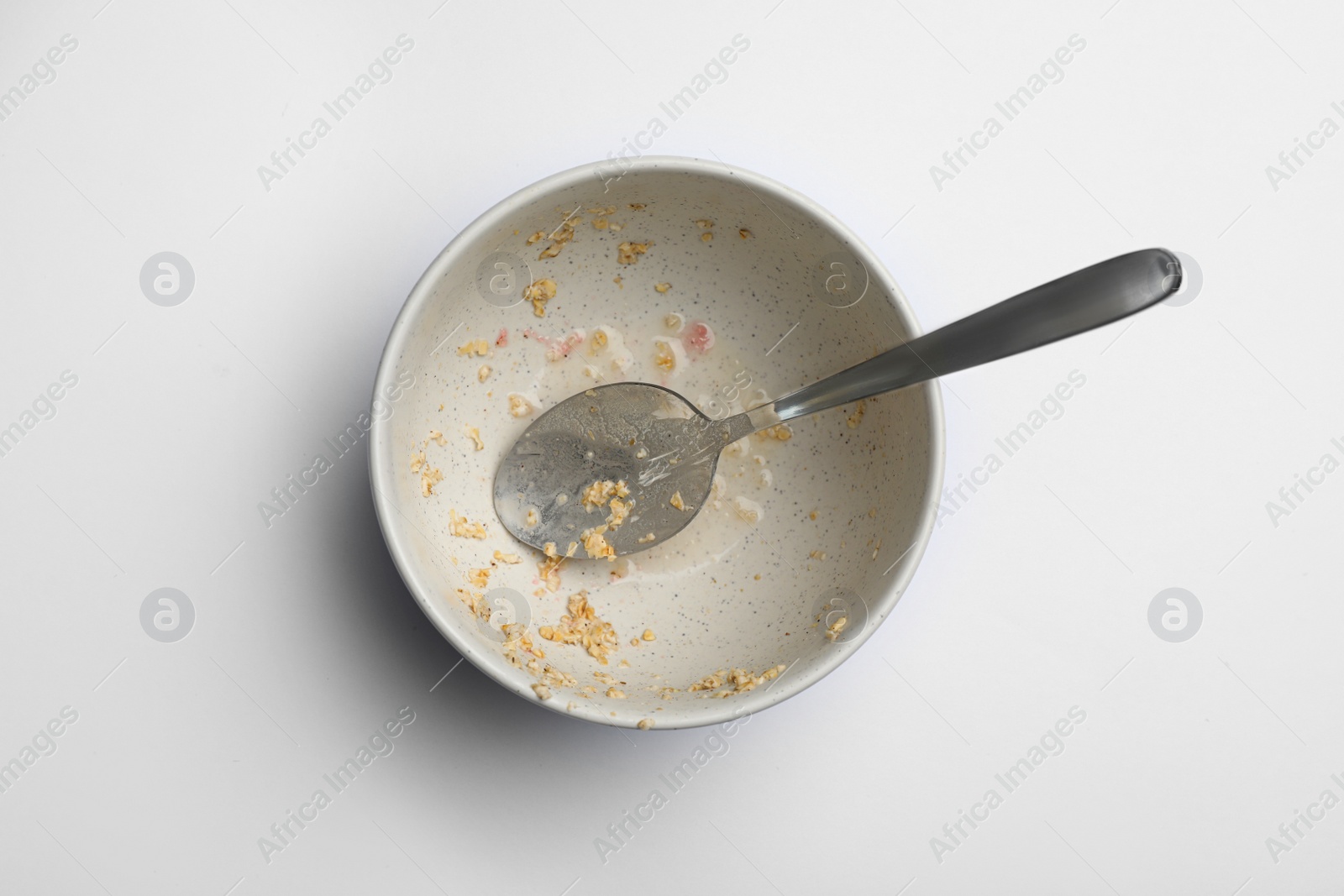 Photo of Dirty bowl with food leftovers and spoon on white background, top view