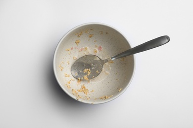 Dirty bowl with food leftovers and spoon on white background, top view