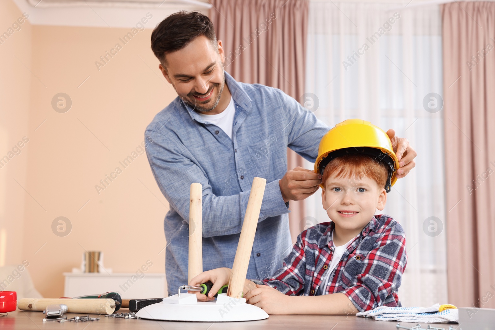 Photo of Father putting hard hat on his son at home. Repair work