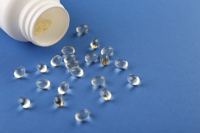 Photo of Bottle and vitamin capsules on blue background, closeup. Space for text