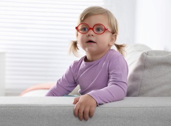 Photo of Cute little girl in glasses on sofa at home. Space for text