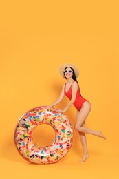 Photo of Happy young woman with beautiful suntan, hat, sunglasses and inflatable ring against orange background, space for text