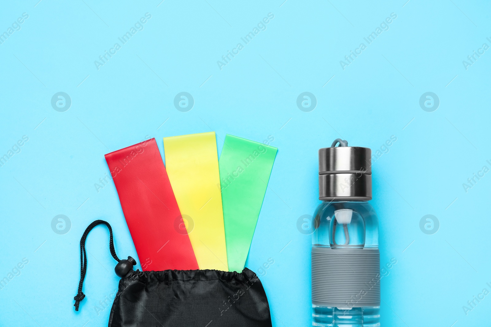 Photo of Set of fitness elastic bands and water bottle on light blue background, flat lay. Space for text