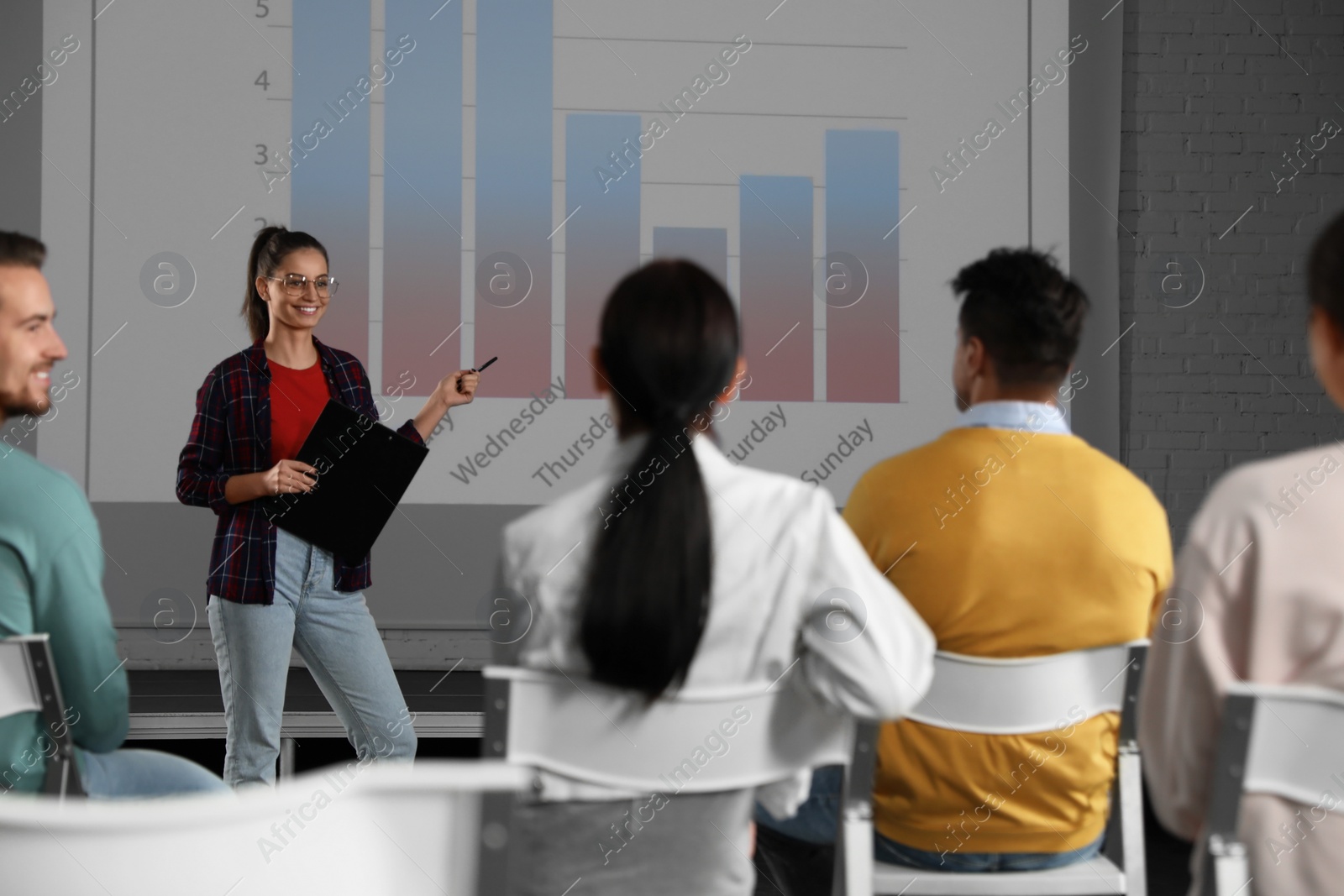 Photo of Female business trainer giving lecture in conference room with projection screen