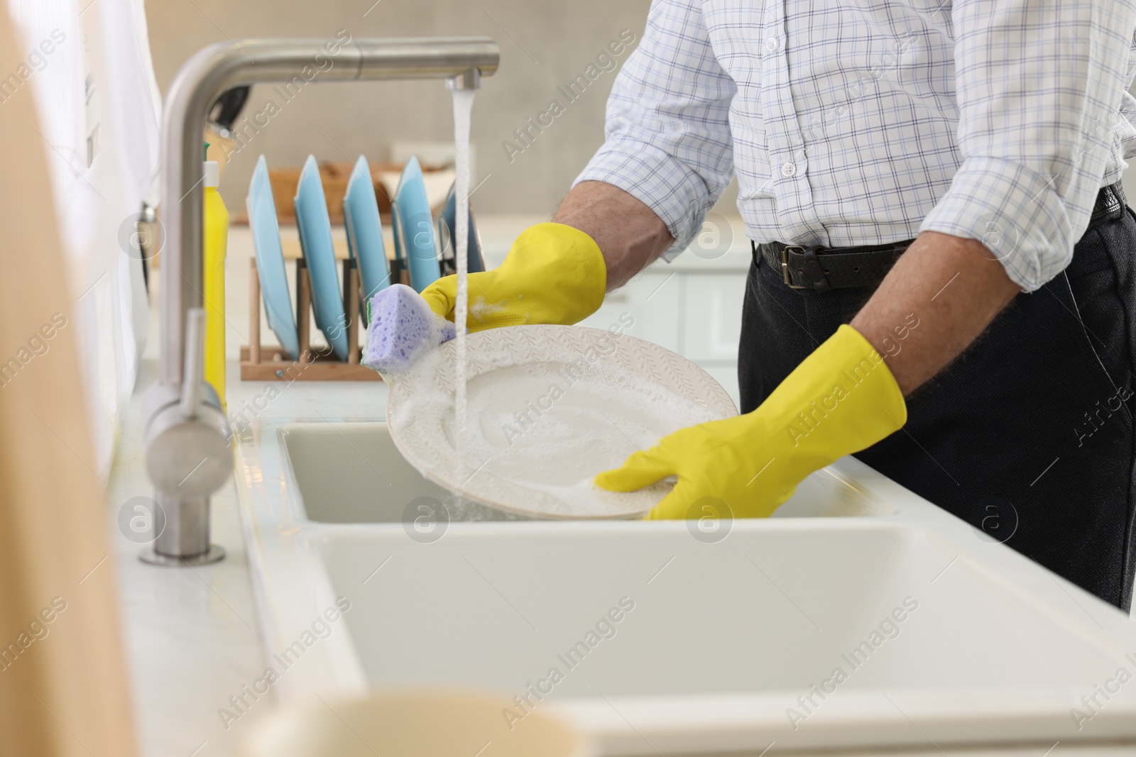 Photo of Man in protective gloves washing plate above sink in kitchen, closeup