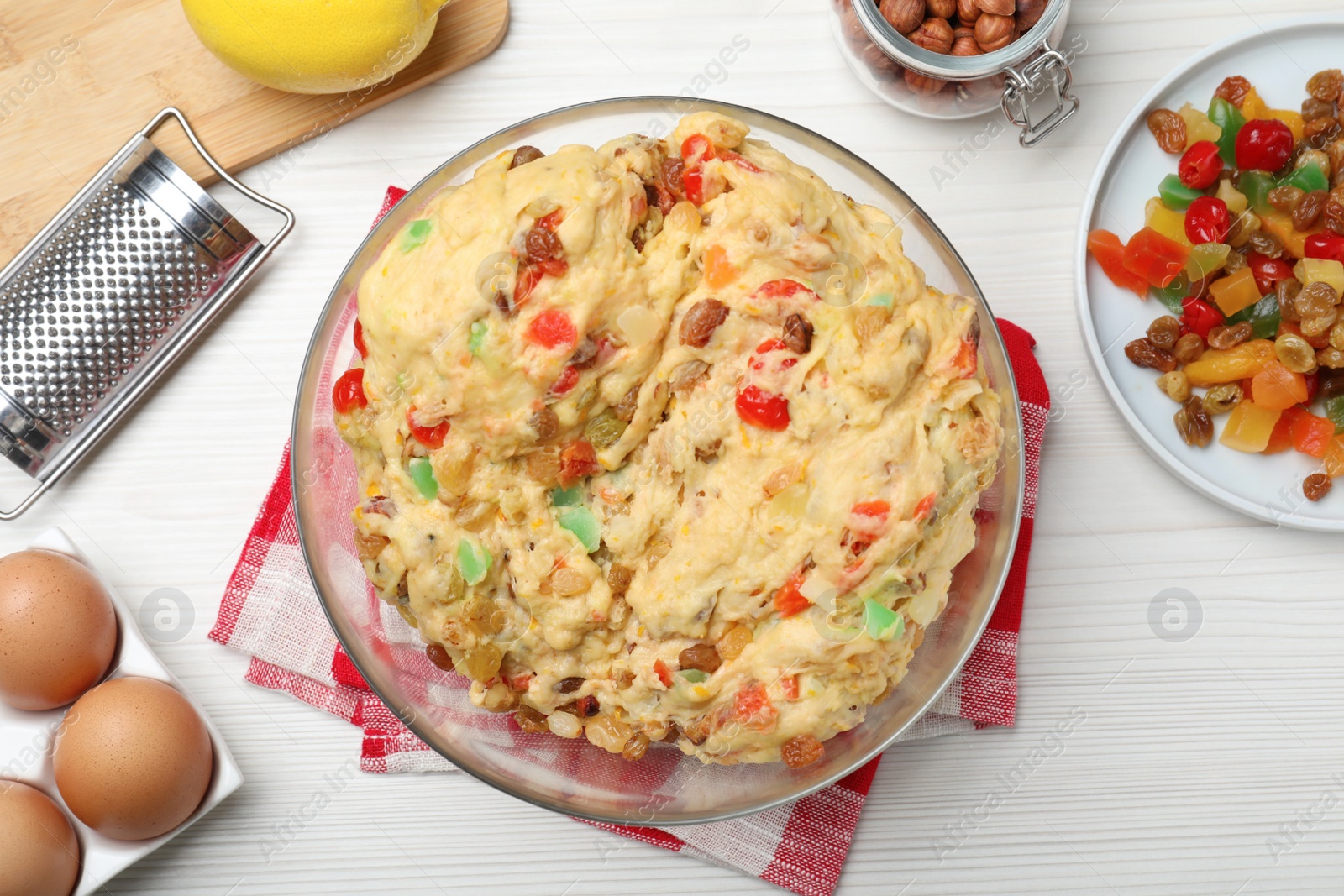 Photo of Raw dough with candied fruits and nuts for Stollen surrounded by ingredients on white wooden table, flat lay. Baking traditional German Christmas bread