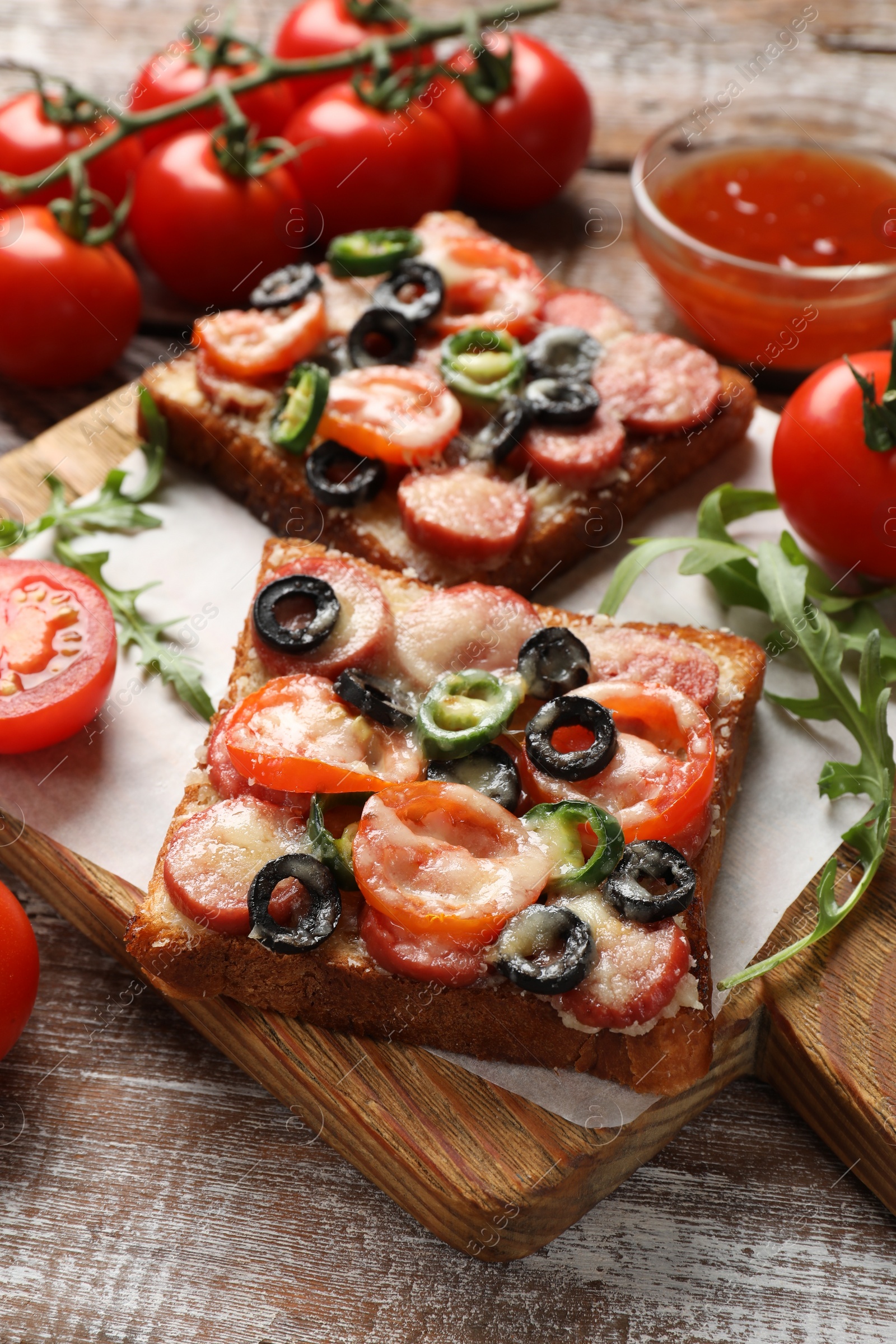 Photo of Tasty pizza toasts, sauce, tomatoes and arugula on wooden table