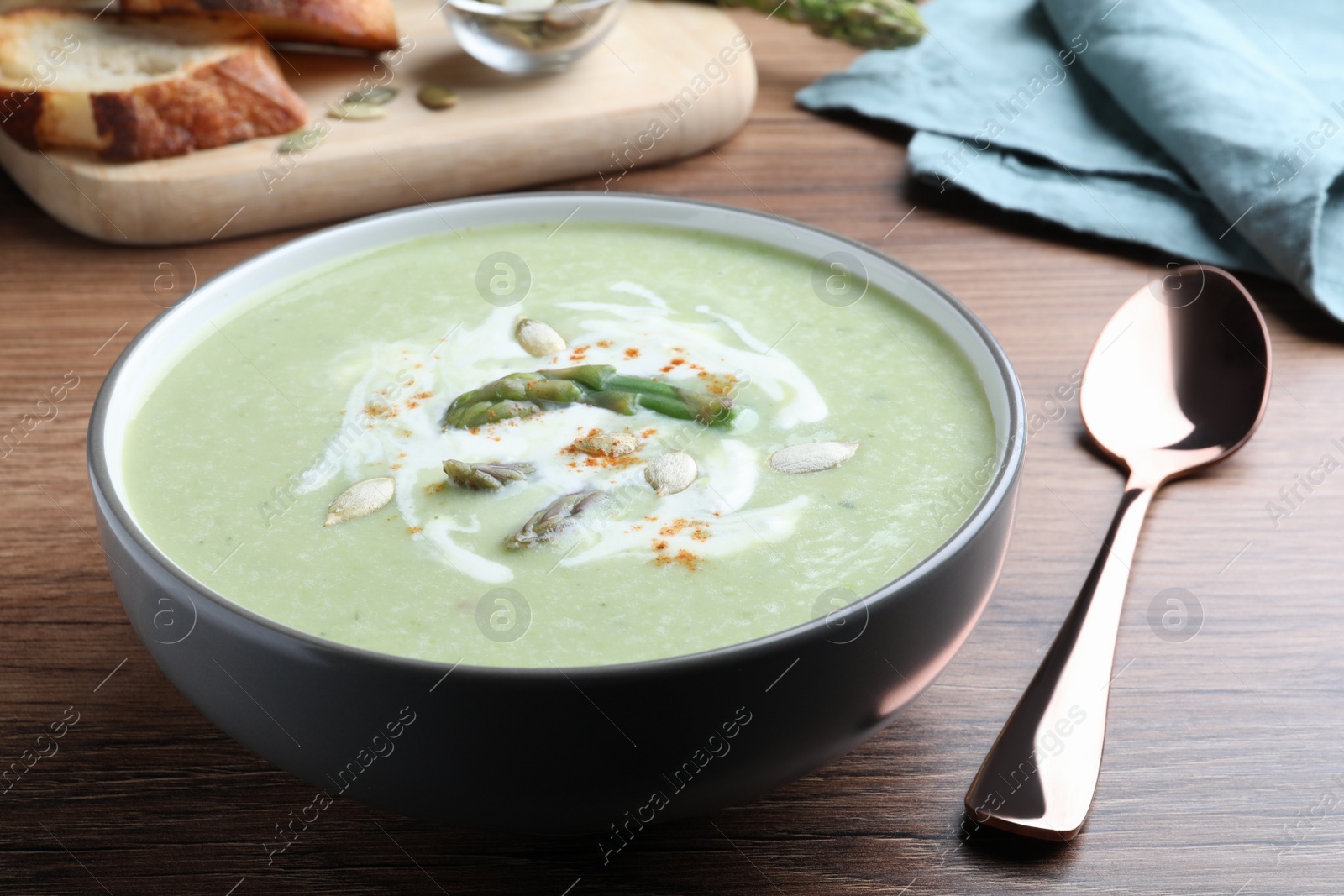 Photo of Delicious asparagus soup with pumpkin seeds served on wooden table, closeup