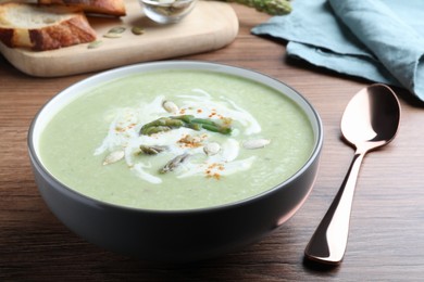 Photo of Delicious asparagus soup with pumpkin seeds served on wooden table, closeup