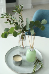Photo of Eucalyptus branches, candle and aromatic reed air freshener on white table indoors. Interior elements