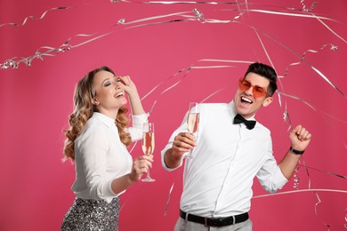 Photo of Happy couple with champagne and falling down serpentines on pink background