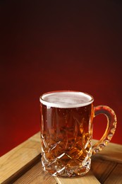 Photo of Mug with fresh beer on wooden crate against burgundy background