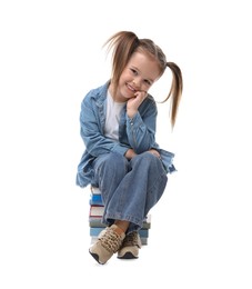 Photo of Cute little girl sitting on stack of books against white background