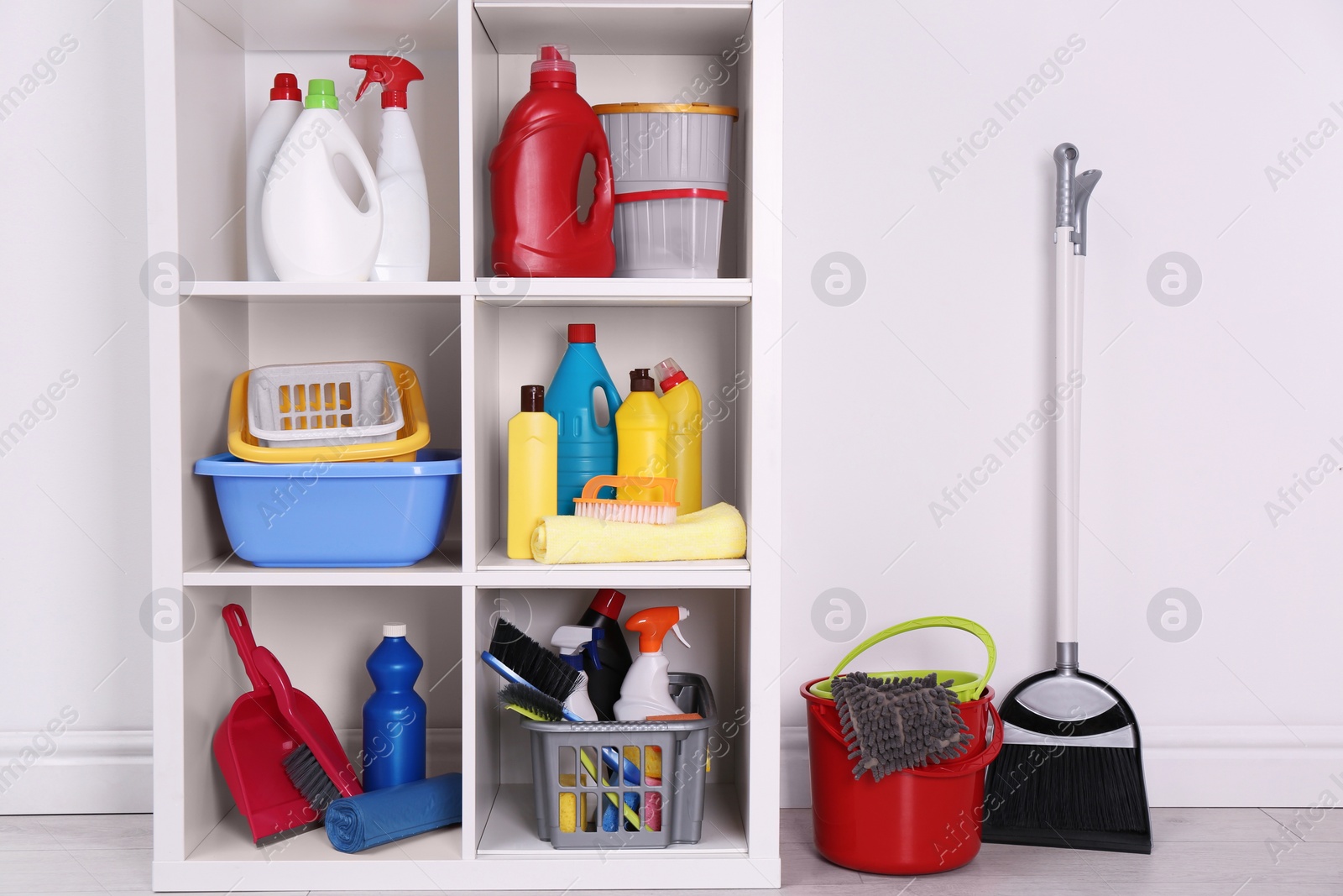 Photo of Shelving unit with detergents and cleaning tools near white wall indoors