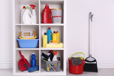 Photo of Shelving unit with detergents and cleaning tools near white wall indoors