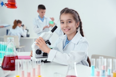 Schoolgirl with microscope at table in chemistry class
