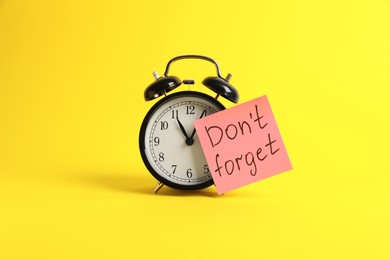 Alarm clock and reminder note with phrase Don't forget on yellow background