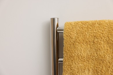 Photo of Heated rail with yellow towel on white wall, closeup. Space for text