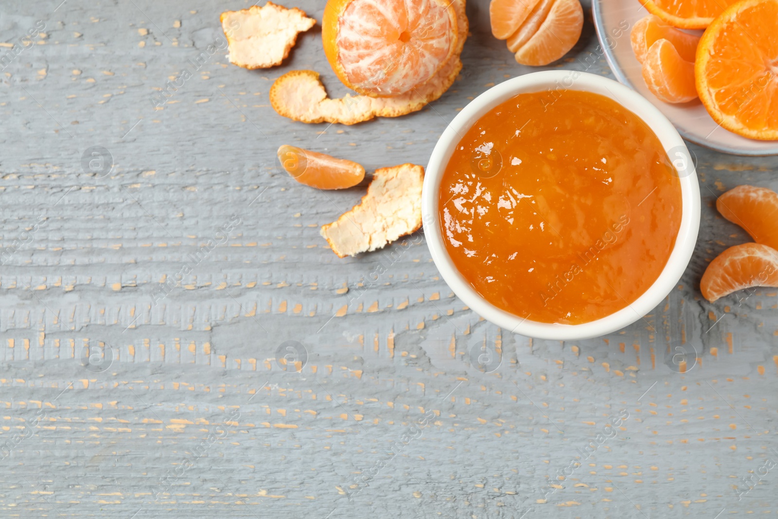 Photo of Flat lay composition with tasty tangerine jam on grey wooden table. Space for text