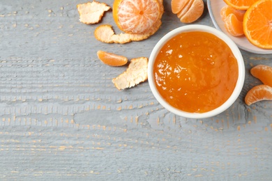 Flat lay composition with tasty tangerine jam on grey wooden table. Space for text