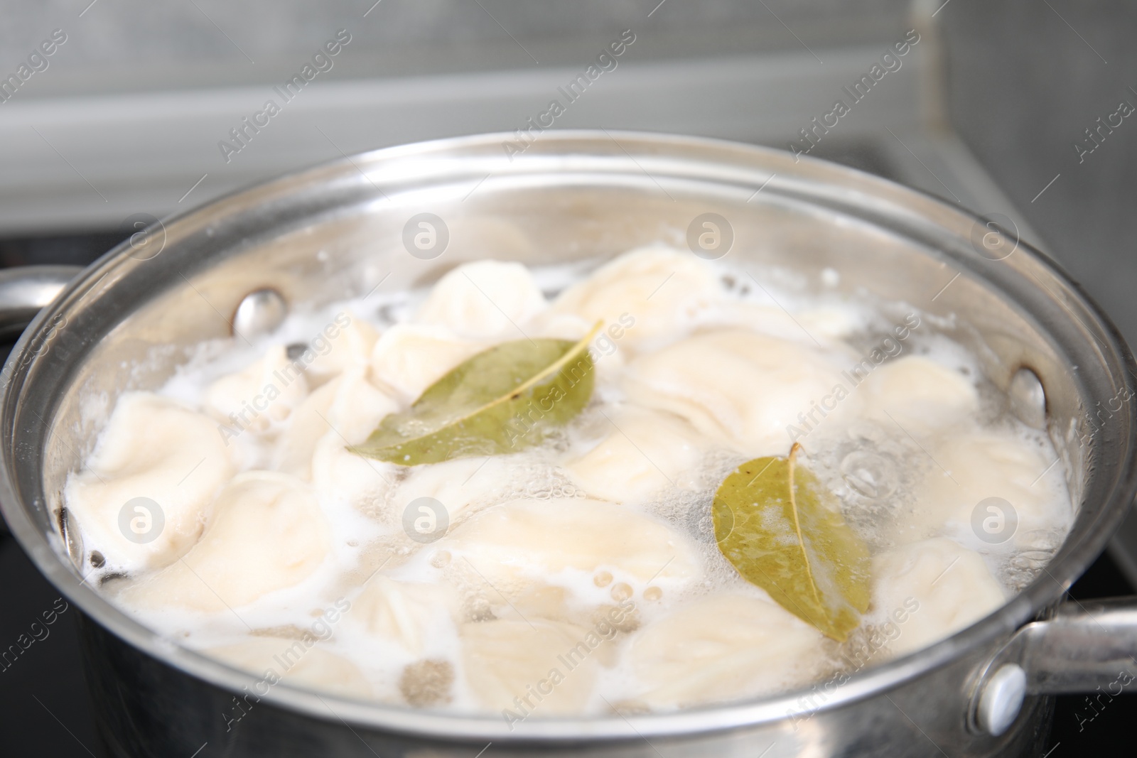 Photo of Cooking dumplings (varenyky) with tasty filling and bay leaves in pot indoors, closeup