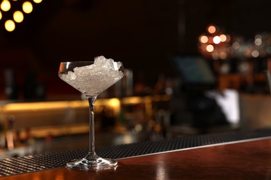 Martini glass with ice on bar counter, space for text