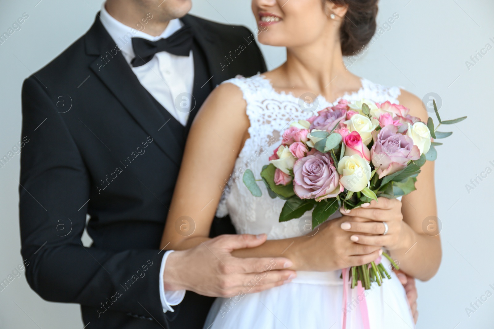 Photo of Young handsome groom and beautiful bride with bouquet on light background