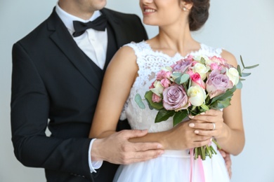 Young handsome groom and beautiful bride with bouquet on light background