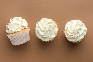 Photo of Tasty vanilla cupcakes with cream on dark beige background, top view