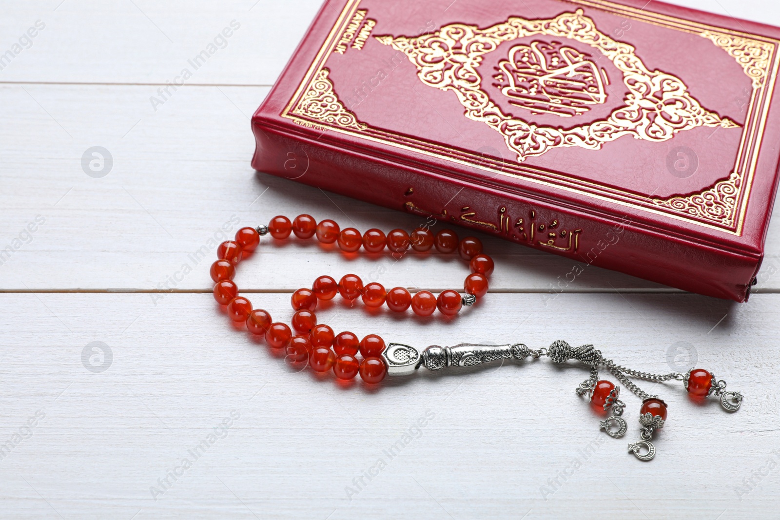 Photo of Muslim prayer beads and Quran on white wooden table, closeup