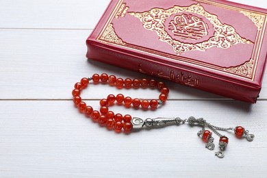 Muslim prayer beads and Quran on white wooden table, closeup