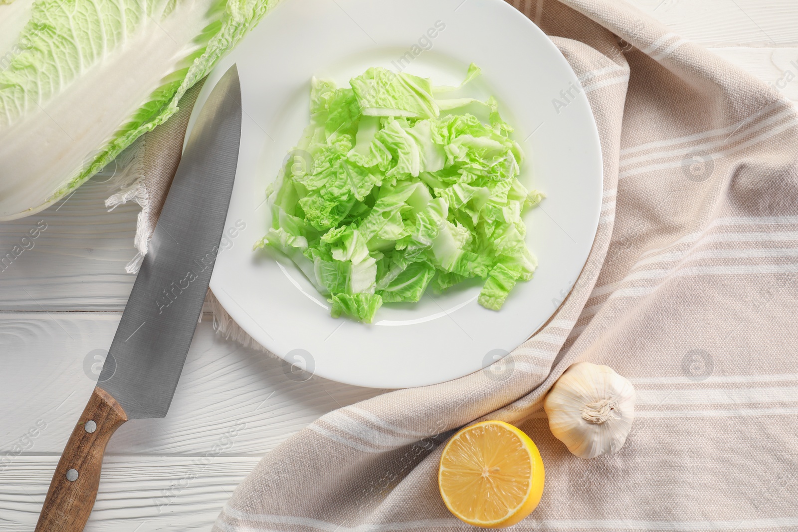 Photo of Cut fresh Chinese cabbage, lemon, garlic and knife on white wooden table, flat lay