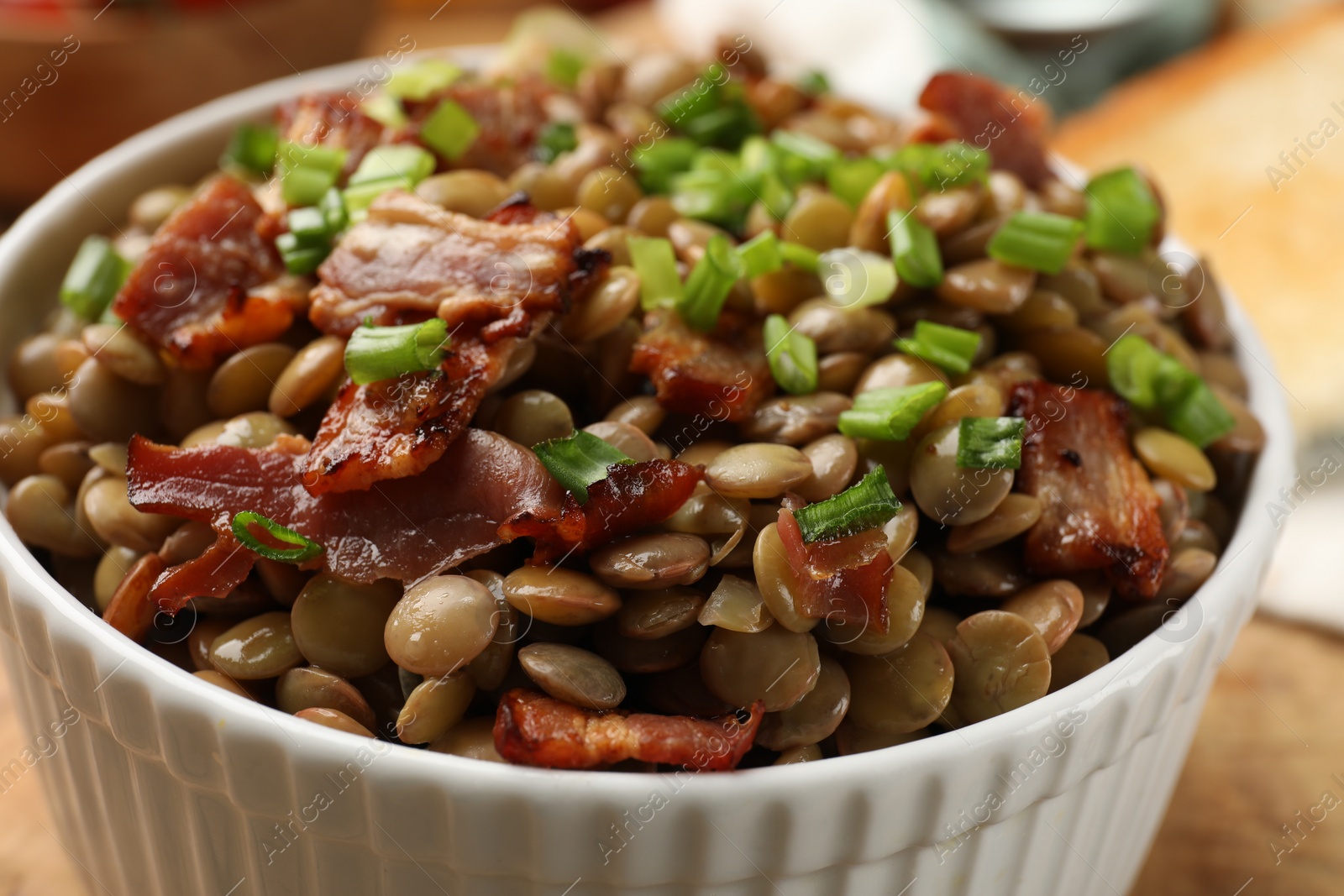 Photo of Delicious lentils with bacon and green onion in bowl, closeup